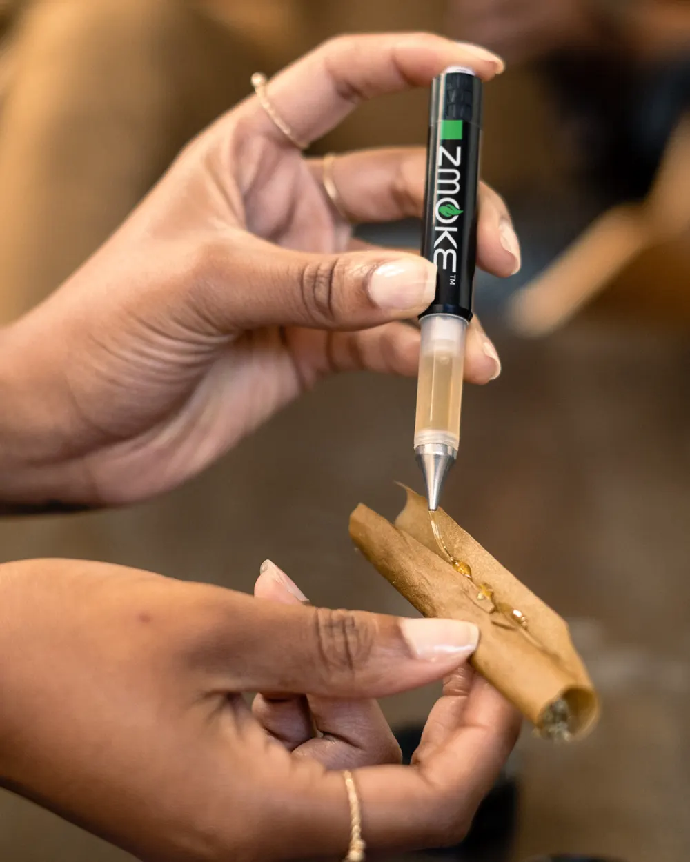 A ZMOKE applicator laying a line of concentrate along an open blunt wrap